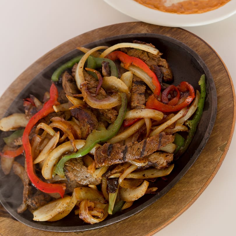 Sizzling steak fajitas with red and green bell peppers and onions on a cast iron skillet.