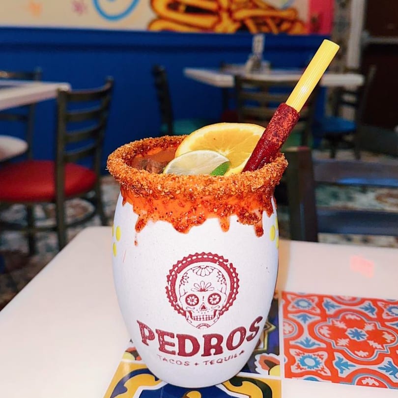 A large Pedros Tacos & Tequila drink with a chili-lime rim, orange, lime, and a tamarind candy straw.