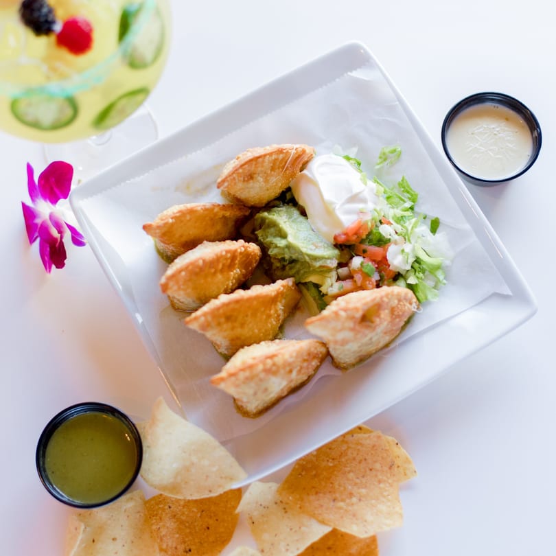 Crispy fried empanadas with guacamole, sour cream, pico de gallo, chips, and sauces, with a margarita.