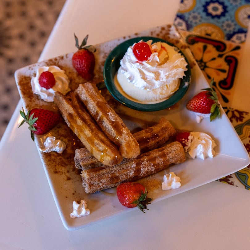Churros with caramel drizzle, cinnamon sugar, whipped cream, strawberries, and vanilla ice cream with a cherry.