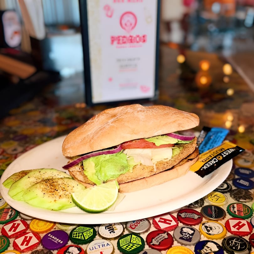 A Pedros Tacos & Tequila sandwich with avocado, lime, and mustard packets on a bottle cap table.